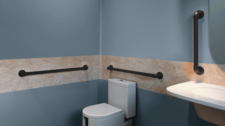 Vista lateral de um banheiro adaptado com paredes azuis e uma faixa decorativa em mármore bege. Instaladas sobre a faixa de mármore, aparecem duas barras de apoio horizontais em PVC de cor preta, posicionadas ao lado e atrás de um vaso sanitário branco com caixa acoplada. À direita, uma terceira barra de apoio preta está fixada verticalmente na parede, próxima a uma bancada branca com pia embutida.