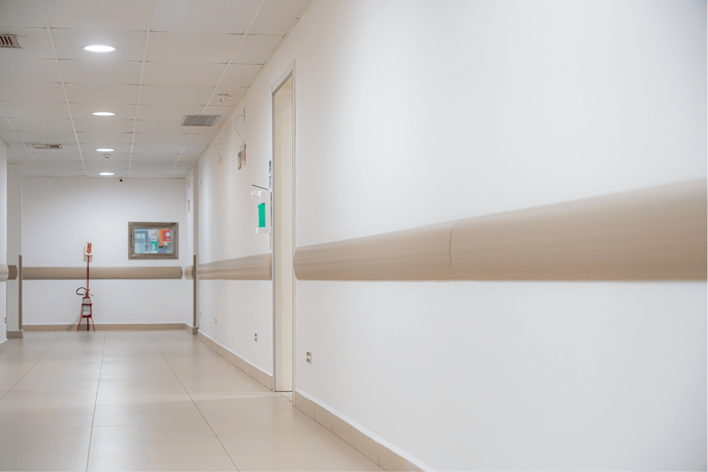 Corredor hospitalar com protetores de parede bege instalados nas laterais para proteção contra impactos.