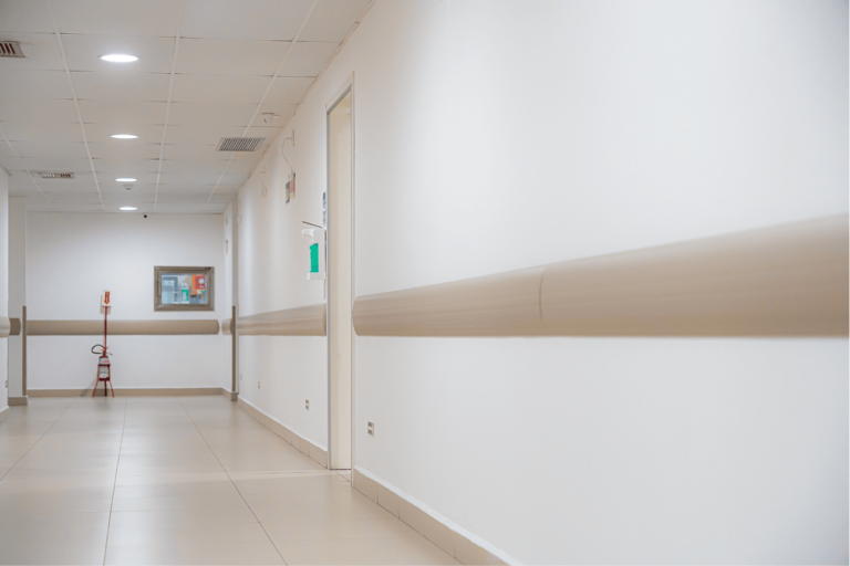 Corredor hospitalar com protetores de parede bege instalados nas laterais para proteção contra impactos.